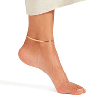 Thumbnail for Layla gold herringbone snake chain anklet worn on tanned ankle with cream knit skirt — 18K gold-plated flat snake chain for everyday wear