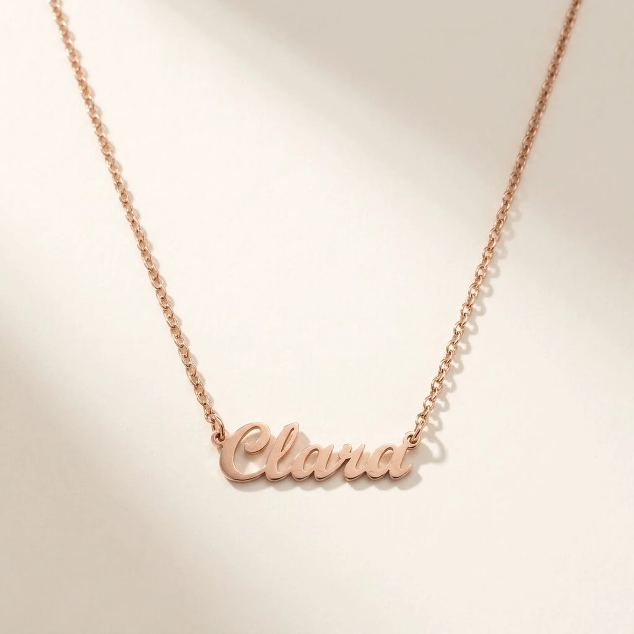 Minimalist Name Necklace in rose gold laid flat, cursive cut-metal script, the name Clara | SKU: minimalistnn-rosegold