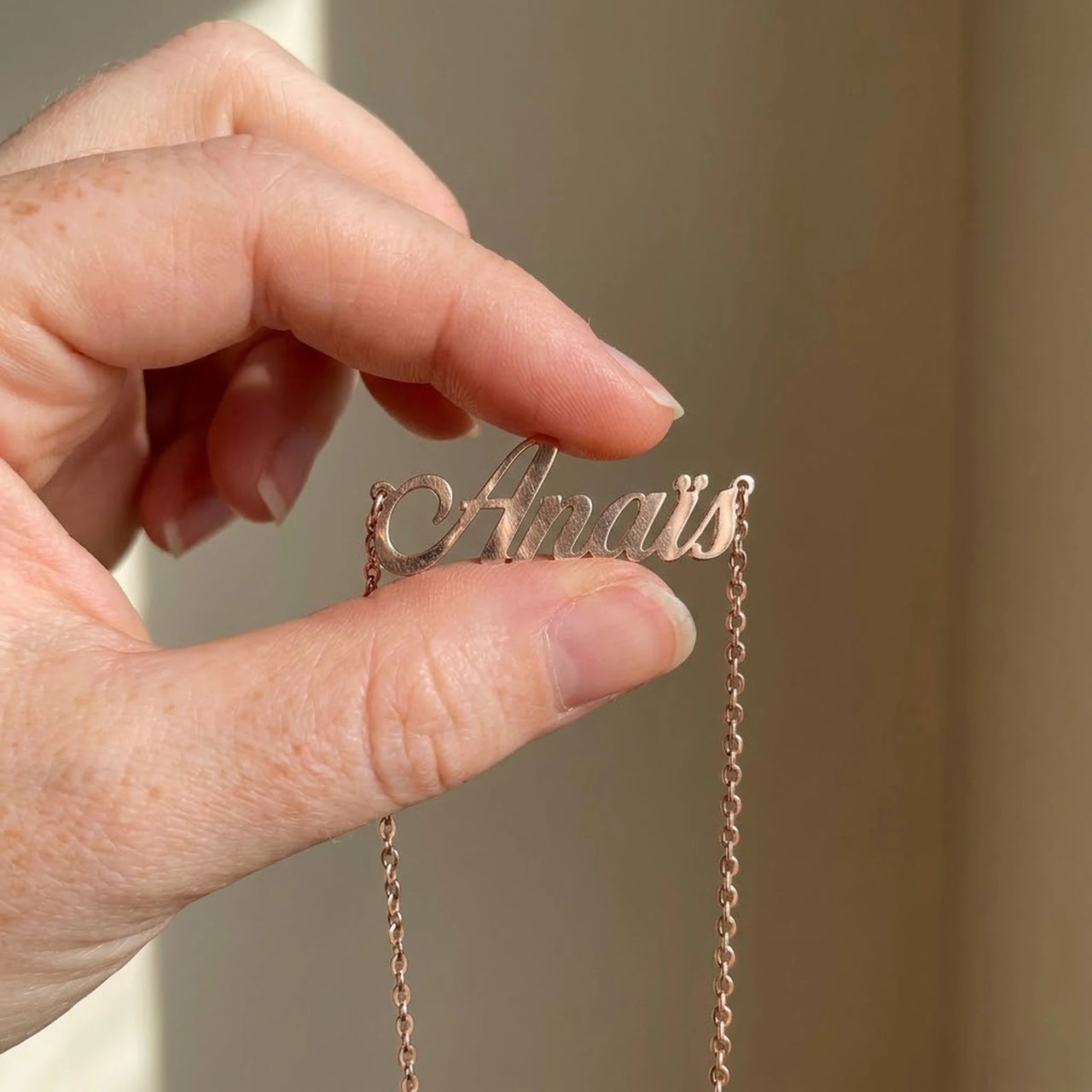 Minimalist Name Necklace in rose gold pendant held between two fingertips showing its true size, the name Anais | SKU: minimalistnn-rosegold