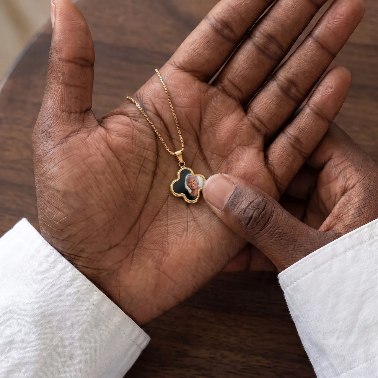 Thumb warming the gold clover pendant: the hidden photo appears under the thumb while the rest stays black | SKU: TPH-CLVN-GOLD