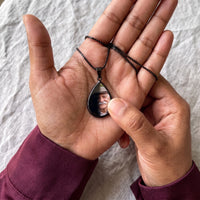 Thumbnail for Thumb warming the black teardrop pendant: the hidden photo appears under the thumb while the rest stays black | SKU: TPH-DRPN-BLACK