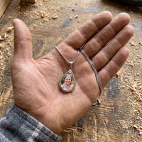 Thumbnail for The silver teardrop photo pendant in a craftsman's open palm over a workbench, showing its real small size | SKU: TPH-DRPN-SILVER